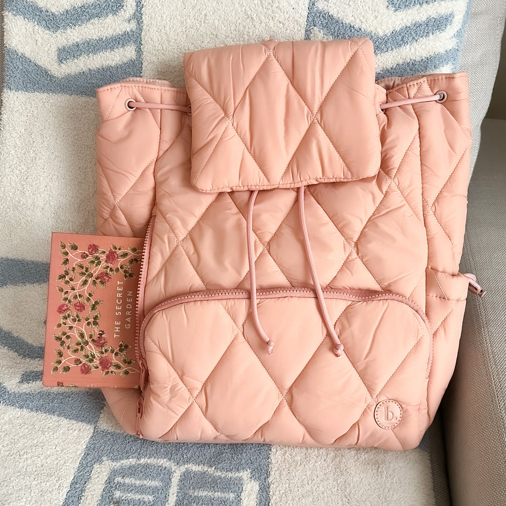The Bookish Backpack in blush pink sitting on a couch with the bookish blanket in blue