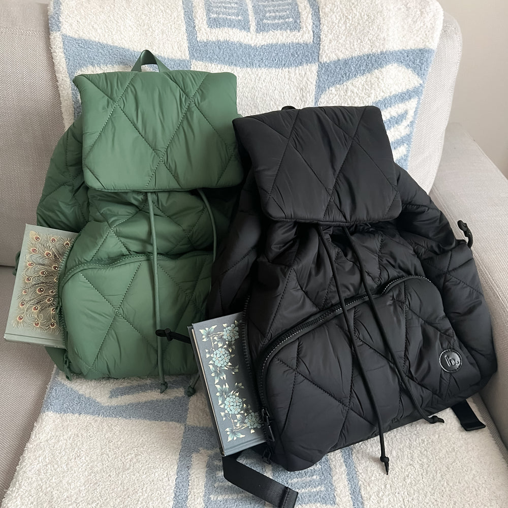 The Bookish Backpack in green and black sitting on a couch with the bookish blanket in blue